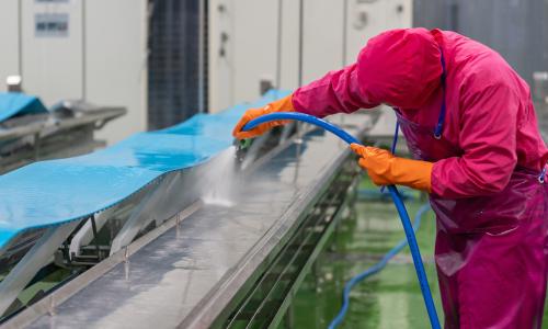 Facility Worker Cleaning Conveyor Belt Using High Pressure Water Spray.